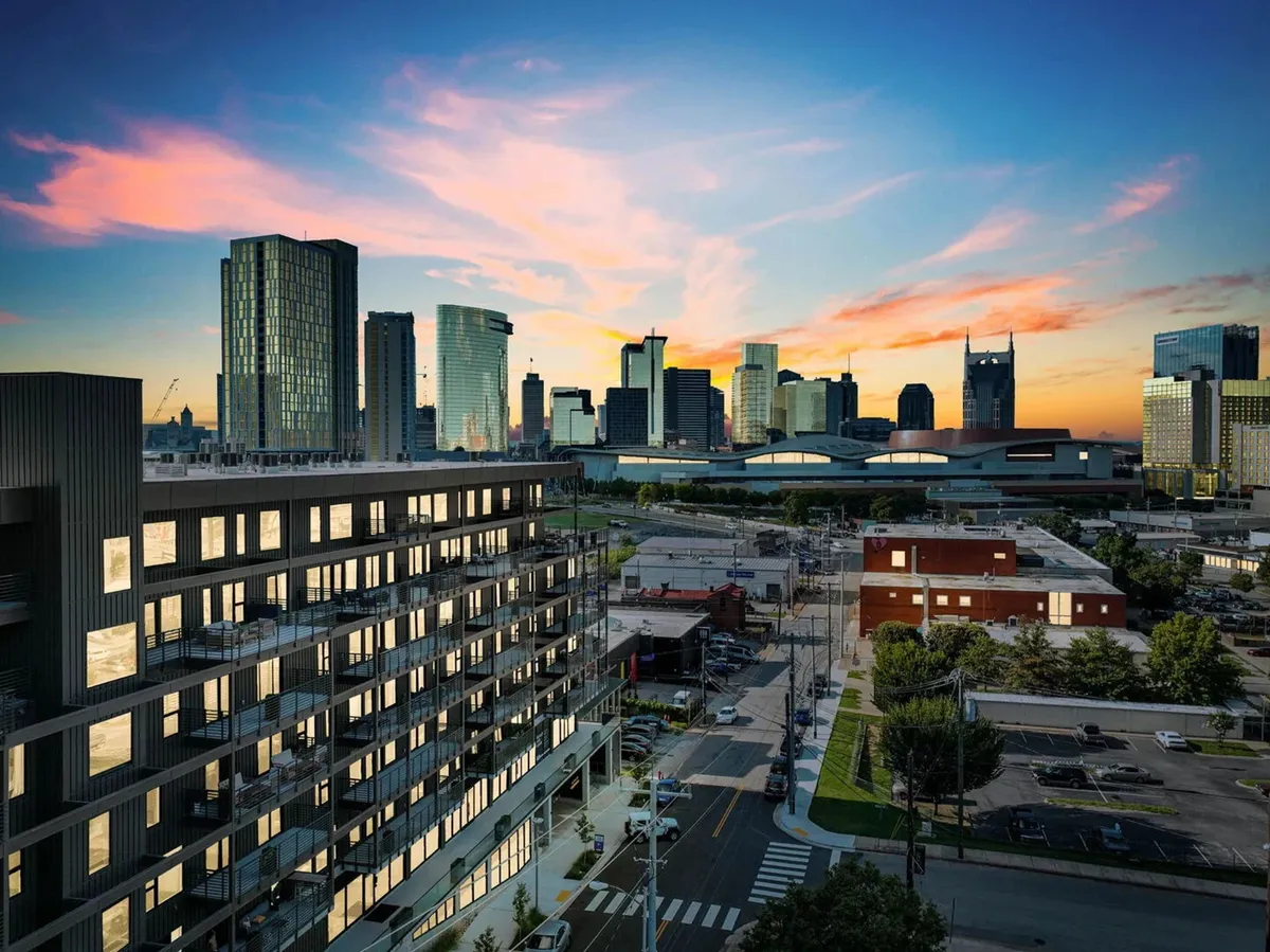 A vibrant shot of a modern apartment building set against Nashville’s dynamic city skyline at sunset. The scene is energetic and urban, highlighting proximity to downtown offices, restaurants, and nightlife.