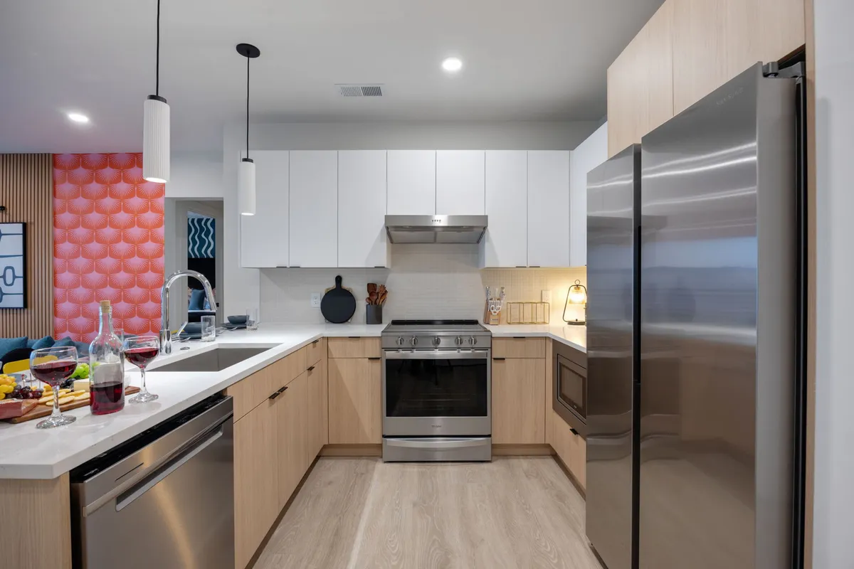 A stylish kitchen scene centered around a spacious island with bar seating. Stainless steel appliances, colorful wall paneling, glassware, and wine bottles create an inviting space for cooking, entertaining, or gathering for a toast. The setup suggests both culinary inspiration and festive possibilities.
