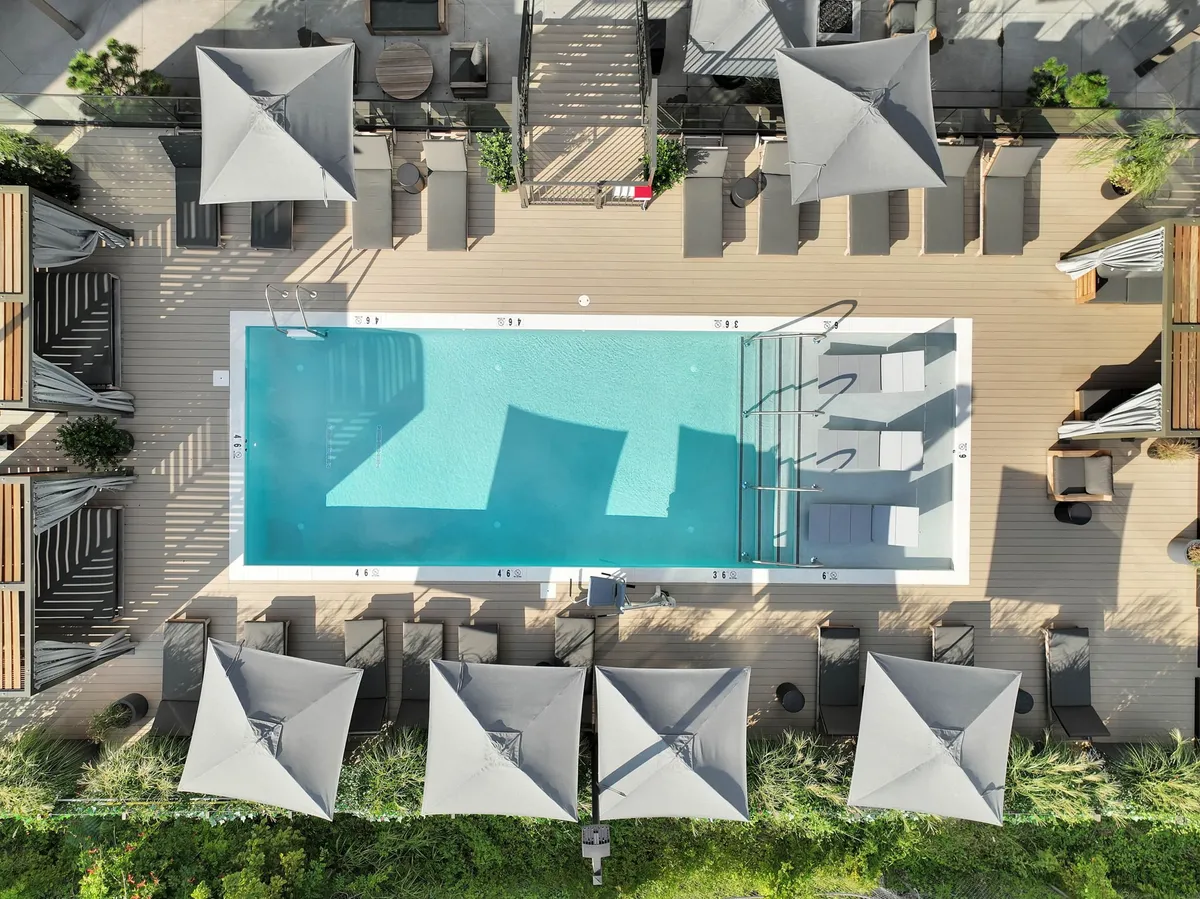 An inviting outdoor pool area with sparkling blue water, surrounded by lounge chairs with umbrellas on a spacious deck. People are seen swimming, sunbathing, and socializing, giving a sense of luxury and relaxation. The ambiance suggests tranquil afternoons and lively poolside gatherings.