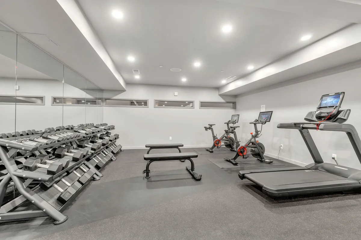 A bright, modern indoor fitness center with a full range of equipment, including treadmills, exercise bikes, a dumbbell rack, and a weight bench. The space is clean and motivational, providing an appealing place for guests to exercise and gather, no matter the weather outside.