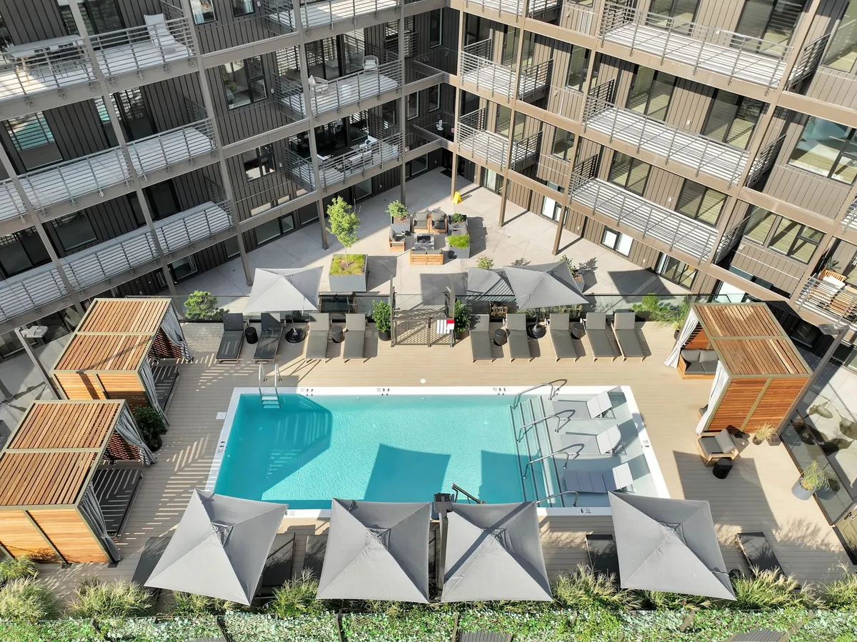 A tranquil pool area featuring lounge chairs, shade umbrellas, lush planters, and a spacious seating area. The environment is serene and ideal for swimming, sunbathing, or relaxing by the water. The setup also suggests flexibility for gatherings, from evening pool parties to quiet afternoons.