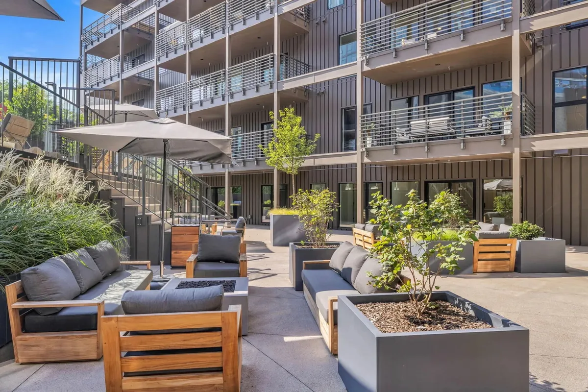 An exterior seating area with planters, greenery, and balconies visible on the building facade. The space offers a welcoming transition from parking and entry, hinting at covered parking and the overall accessibility of the property.