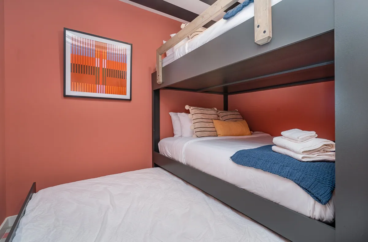 A playful bunk room designed with a bunk bed, plush bedding, and colorful artwork, creating a cozy and inviting space ideal for kids or friends to unwind, play, or share bedtime stories.