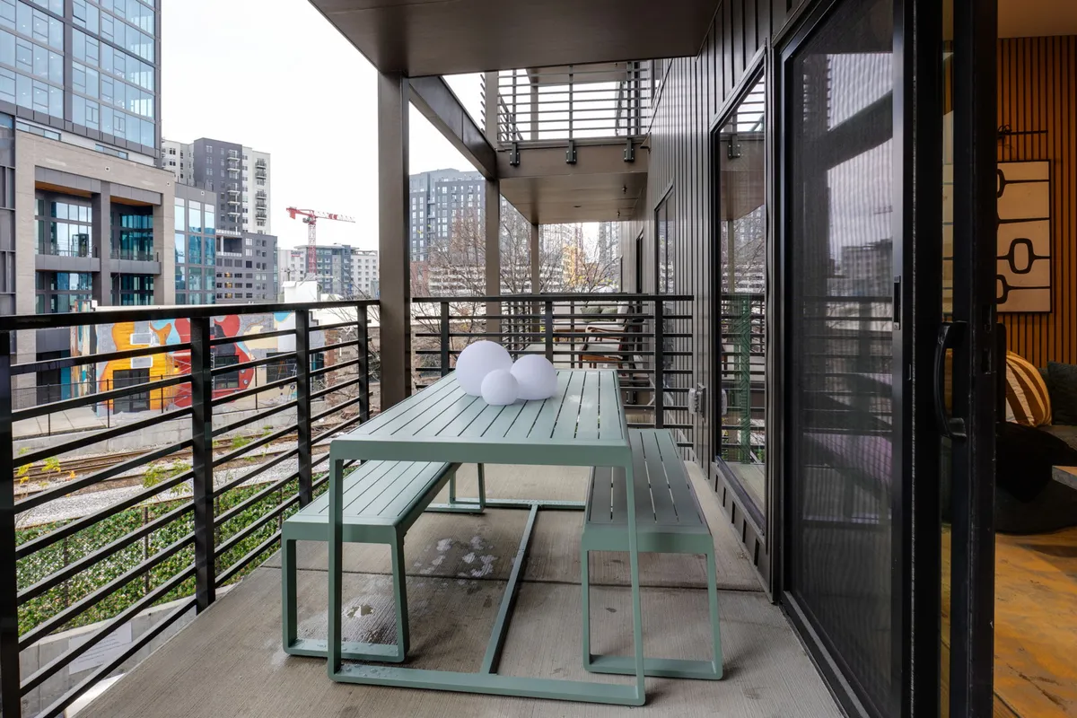 This image shows a contemporary outdoor seating area with a green table, decorative white objects, and a view of the urban landscape beyond. The setup is ideal for relaxing, socializing, or enjoying a meal outdoors.
